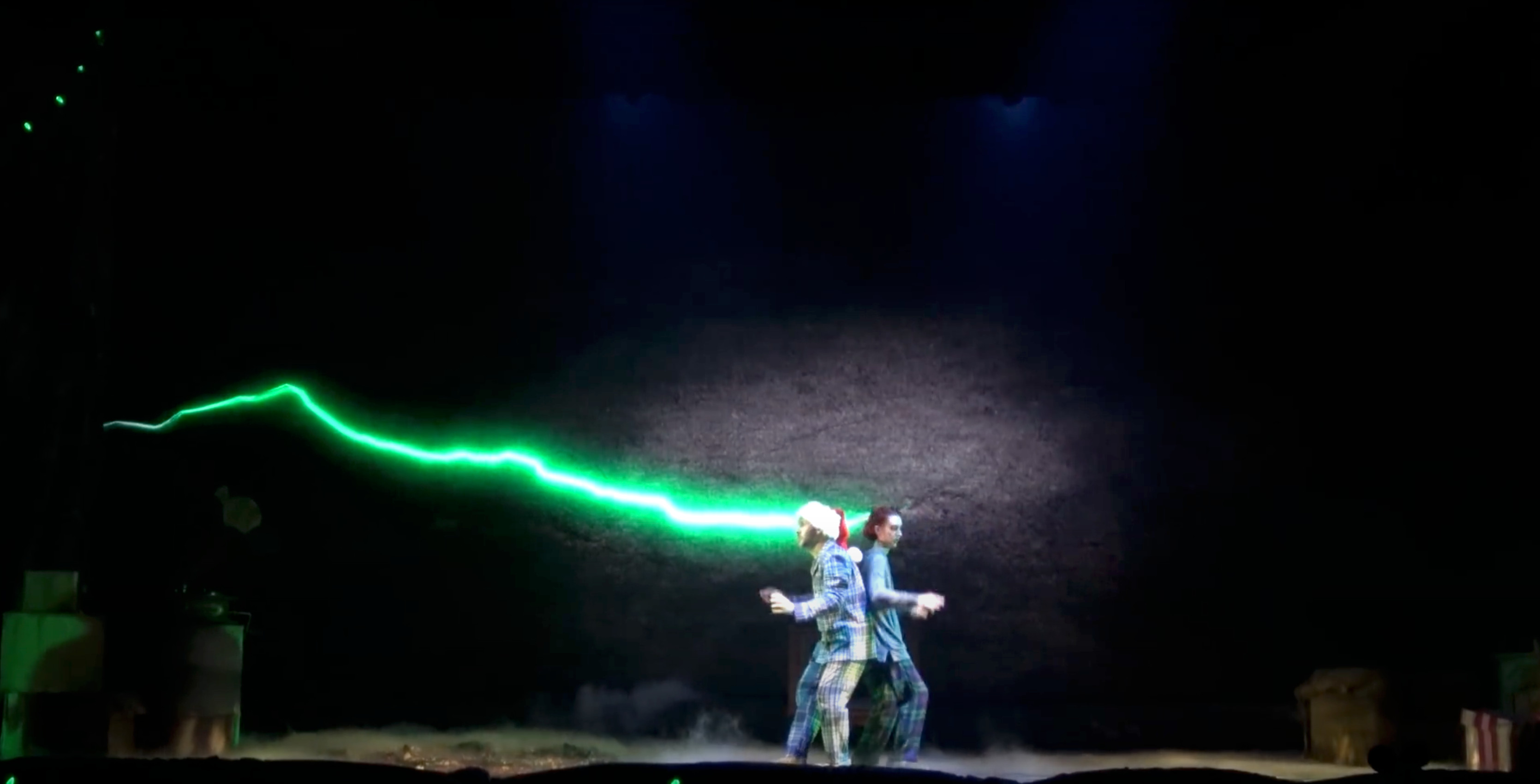 As the performers move towards the center of the stage, the crack grows brighter and the screen darkens as if the wall itself is about to consume the performers